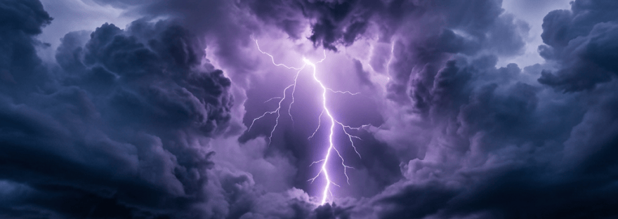 Lightning strikes beneath dark storm clouds over a rugged coastline and mountain range